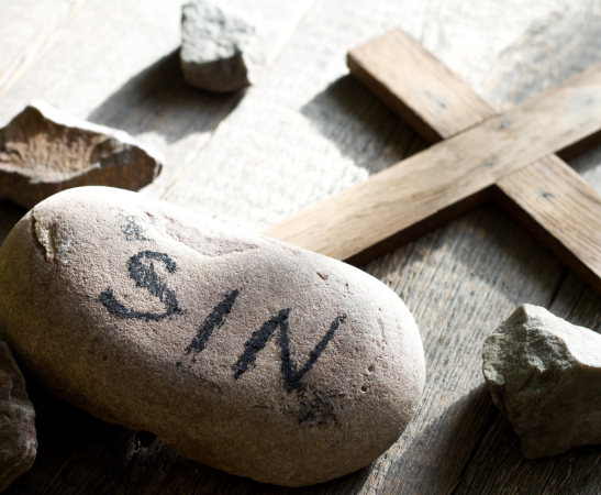 Sin written on a stone with a cross behind it
